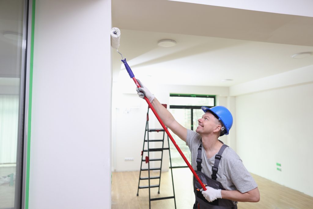 Smiling decorator in helmet painting wall with roller brush