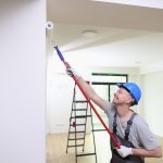 Smiling decorator in helmet painting wall with roller brush