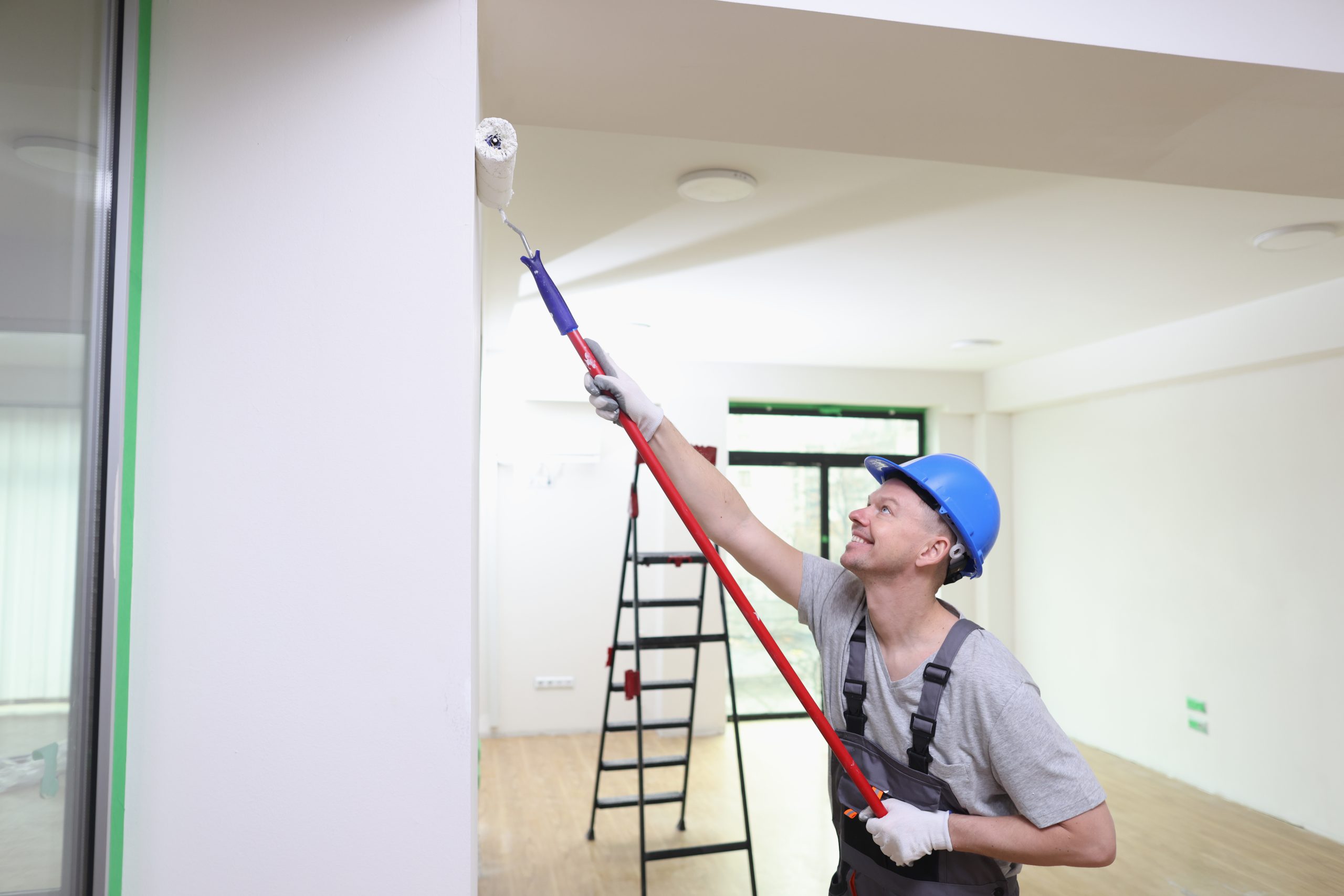Smiling decorator in helmet painting wall with roller brush